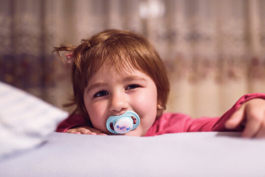 a little girl with a pacifier posing in her room.