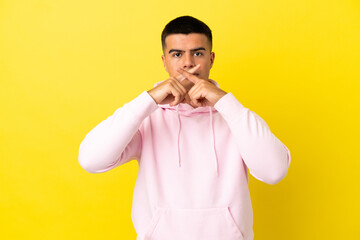 Young handsome man over isolated yellow background showing a sign of silence gesture