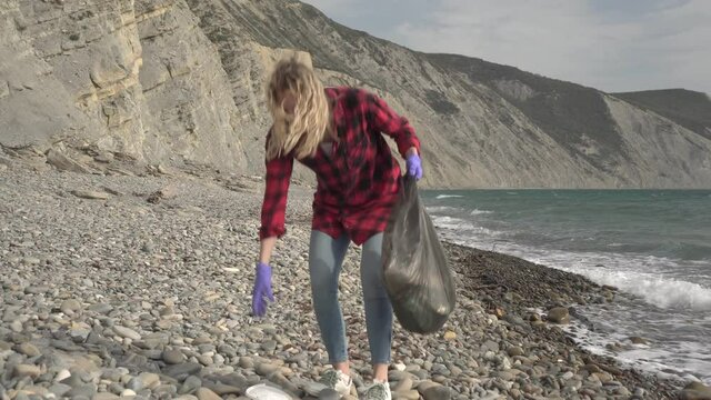 Volunteer ecologist person removes rubbish on the beach. A woman cleans the sea shore from garbage