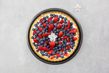 Delicious blueberry and strawberry tart with whipped cream and mascarpone on a light gray concrete...