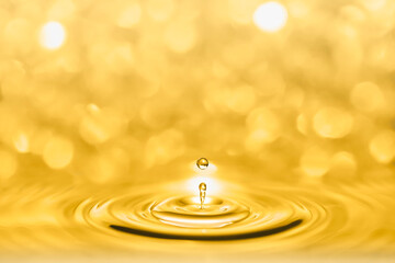 Macro photography of a droplets splash of golden liquid shining and creating circular waves on a...