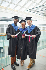 Vertical full length view at diverse group of college graduates holding diploma certificates and...