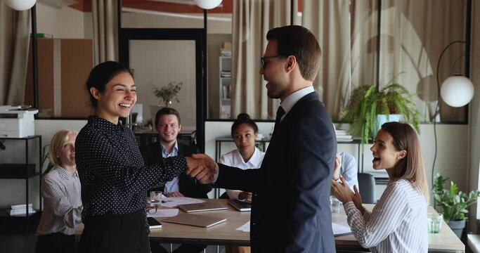 Smiling confident male ceo executive manager leader praising supporting happy young excited indian female colleagues at meeting with diverse teammates, shaking hands thanking for good job or promoting