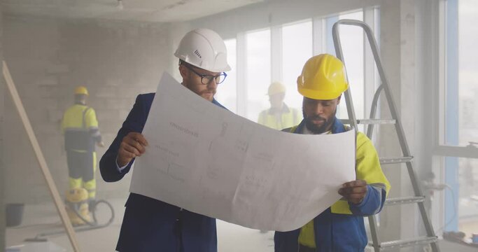Young engineer discussing blueprint with building worker on construction site.