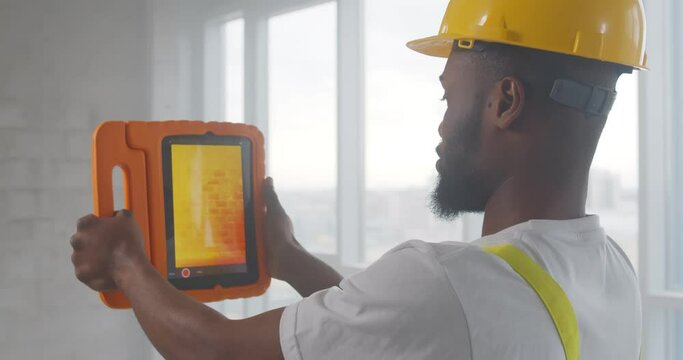 African builder doing analysis of heat on wall with thermal imaging camera