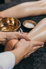 Female hands massaging the leg with oils. Gold body treatment and diamond powder exfoliating scrub.