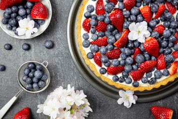 Delicious blueberry and strawberry tart with whipped cream and mascarpone on a dark stone background. Top view. Close up.
