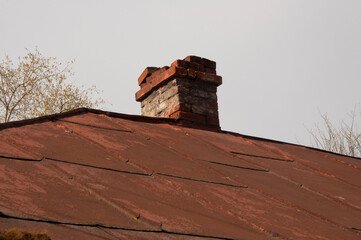 one old large brick chimney on roof of a private house on background blue sky