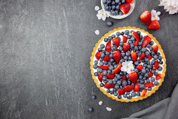 Delicious blueberry and strawberry tart with whipped cream and mascarpone on a dark stone background. Top view. Copy space.