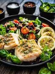 Fish dish - fried cod fillet with fresh vegetable salad on wooden table
