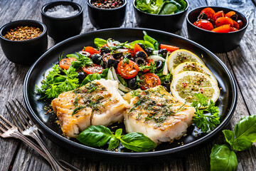 Fish dish - fried cod fillet with fresh vegetable salad on wooden table

