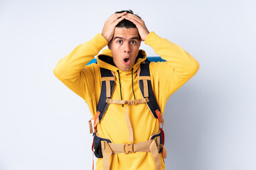Young mountaineer man with a big backpack over isolated blue background with surprise facial expression