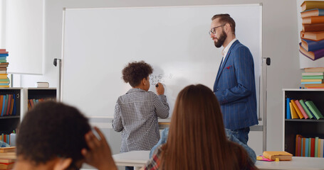 Little african schoolboy writing numbers on white board in classroom