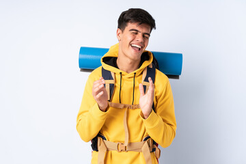 Young mountaineer man with a big backpack over isolated blue background laughing