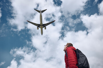 Young man looking up at flying airplane against cloudy sky. Themes nostalgia for travel and aviation. © Chalabala