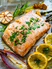 Sheet pan dinner - roasted salmon steak with asparagus, lemon ,rosemary, tomatoes, onion and garlic on cooking pan on wooden table
