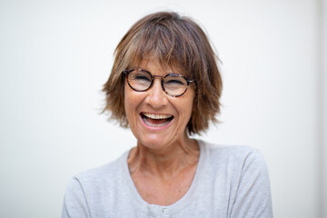 Close up older woman laughing with eyeglasses by white background