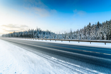 Clear winter day, an empty country road passing through the coniferous forest. View from the side of the road