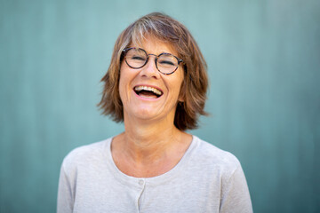 Close up woman in 50s laughing by green background