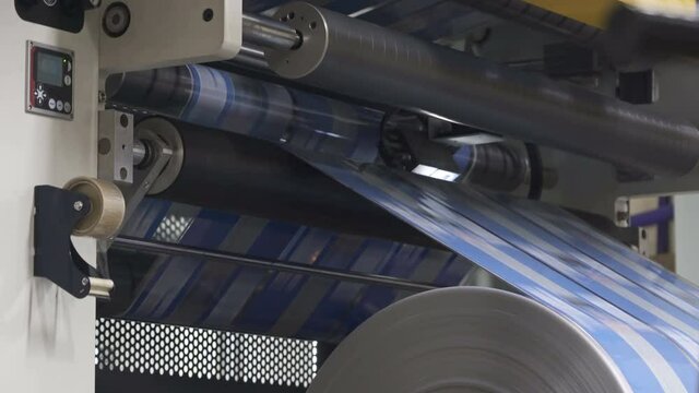 Flexo printing. Printing house. Shaft rotates rapidly. Film spins on shafts. Rroller machine prints. Anilox shafts