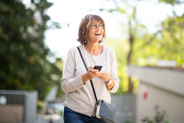 happy older woman laughing with mobile phone outside
