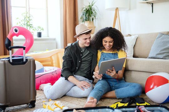 Young Couple With Tablet Packing For Holiday At Home.