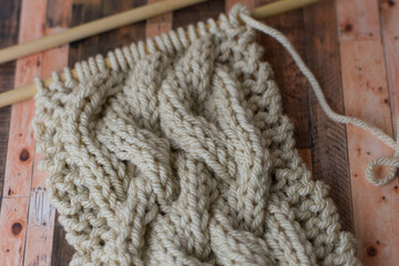 close up of knitting needles with cable pattern on beige yarn 