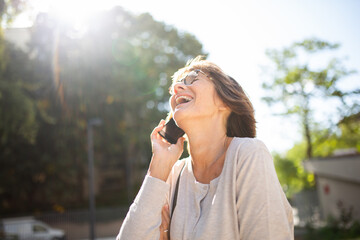 older woman laughing with mobile phone outside