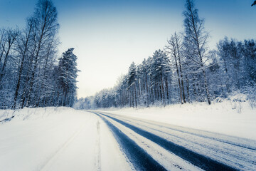 Snowfall on a winter day, snow-covered country road. View from the side of the road. Coniferous forest. Russia, Europe. Beautiful nature.