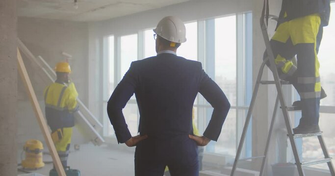 Back view of contractor in suit and hardhat supervising team of builders renovating office