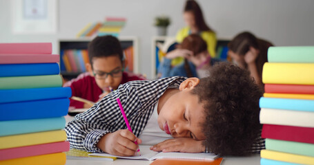 Tired african child sleeping while studying in the primary school classroom.