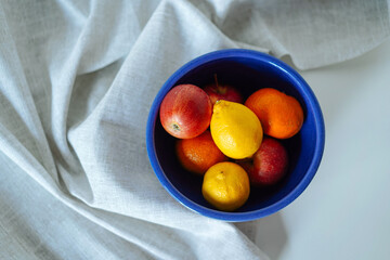 Healthy fruits in blue ceramic bowl on table with grey linen cloth. Natural vitamins to strengthen the immune system