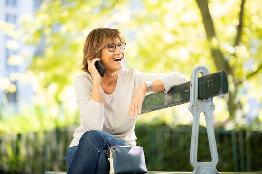 happy older woman sitting on park bench talking with cellphone