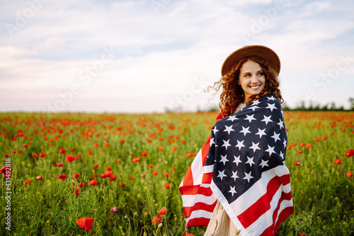 Young woman in hat with the American flag in in the poppy field. Fourth of July. Freedom. Beautiful sunset. Independence Day. Patriotic holiday.