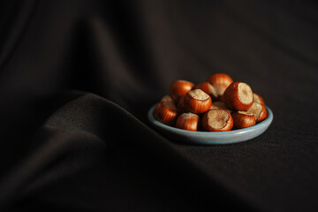 Unpeeled hazelnuts in small plate on black cloth background