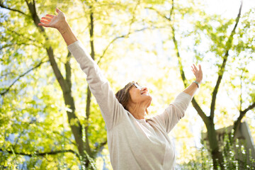 carefree older woman with arms up in park