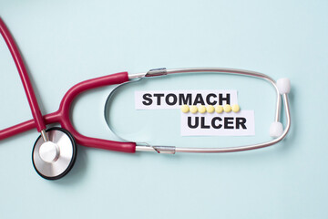 The word ulcer is on a white label among the pills and a stethoscope. Medical concept