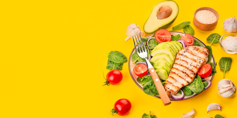 Grilled chicken breast and fresh vegetable salad with spinach leaves, avocado and tomatoes on a yellow background. Salad of greens with meat. Ketogen diet. Dietary nutrition. View from above. 