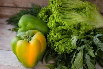 The concept of healthy eating. Green dill leaves and arugula, and lettuce along with green bell pepper on a wooden background