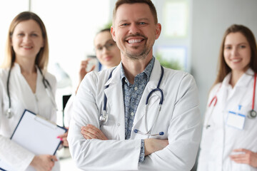 Fototapeta premium Successful smiling man doctor standing against background of colleagues in clinic