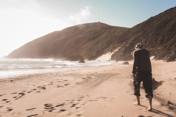 Man walking with his shoes in his hand on the beautiful and mountainous Big Sur Coast of California on a misty yet sunny day, United States of America aka USA.