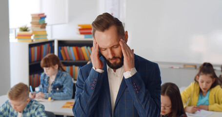 Tired teacher in suit suffering from headache standing in classroom