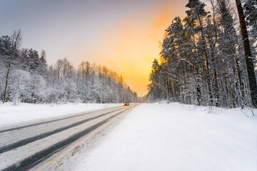 Fototapeta na wymiar Sunrise on a clear winter morning, the headlights of approaching cars on a country road into a snowfall passing through a pine forest. View from the side of the road. Coniferous forest. 