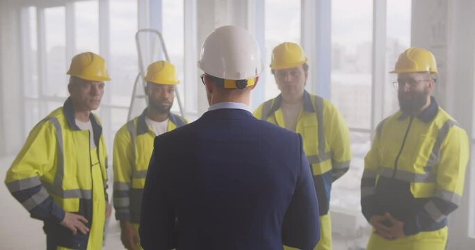 Back view of businessman in suit talking to construction workers team