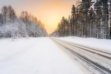 Sunrise on a clear winter morning, road passing through the forest in the snow. View from the side of the road. Coniferous forest. Russia, Europe. Beautiful nature.