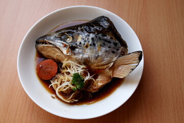Close up braised salmon head with soy sauce or Salmon kabutoni on white round dish and brown wood...