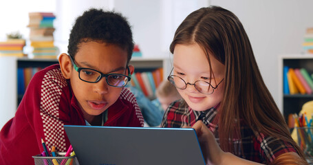 Two preteen diverse students using laptop in classroom - Powered by Adobe