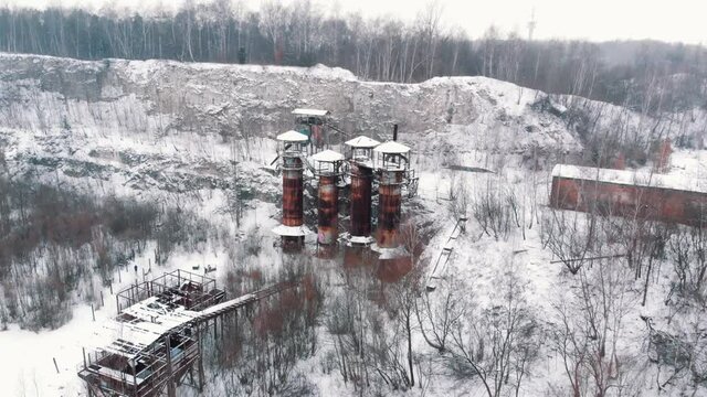 Aerial footage of Old machines and piping equipment in Liban Quarry - A historic site where prisoners were kept during the Second World War. Light snow-fall. Snow-covered trees in the background. 