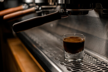 transparent glass with coffee on steel surface of professional coffee machine in coffee shop