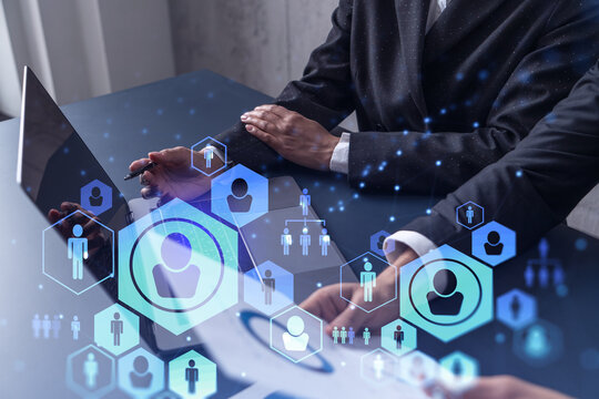 Two HR specialists analyzing the recruitment market using laptop to boost the intern program at international consulting company. Social networking hologram icons.